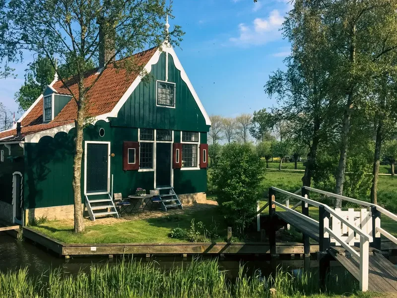 Groen houten boerderijtje aan het water, met een brug ernaartoe over de sloot